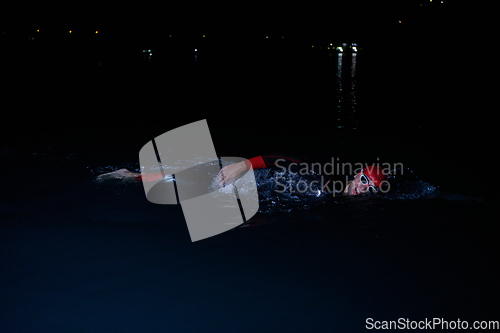 Image of A determined professional triathlete undergoes rigorous night time training in cold waters, showcasing dedication and resilience in preparation for an upcoming triathlon swim competition