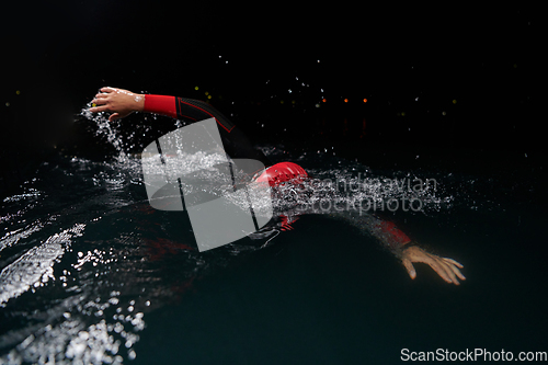 Image of A determined professional triathlete undergoes rigorous night time training in cold waters, showcasing dedication and resilience in preparation for an upcoming triathlon swim competition