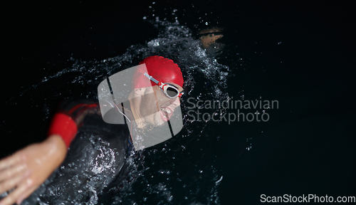 Image of A determined professional triathlete undergoes rigorous night time training in cold waters, showcasing dedication and resilience in preparation for an upcoming triathlon swim competition