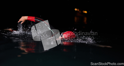 Image of A determined professional triathlete undergoes rigorous night time training in cold waters, showcasing dedication and resilience in preparation for an upcoming triathlon swim competition