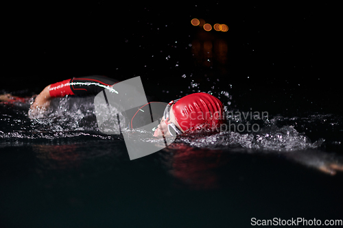 Image of A determined professional triathlete undergoes rigorous night time training in cold waters, showcasing dedication and resilience in preparation for an upcoming triathlon swim competition