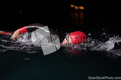 Image of A determined professional triathlete undergoes rigorous night time training in cold waters, showcasing dedication and resilience in preparation for an upcoming triathlon swim competition