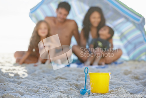 Image of Big family, sand and box on beach with umbrella, spade or bucket for playing on ocean coast. Blue and yellow toys on sandy shore with people for fun bonding, relax or outdoor holiday weekend together