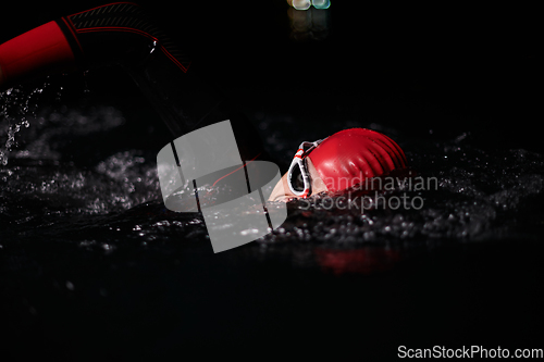 Image of A determined professional triathlete undergoes rigorous night time training in cold waters, showcasing dedication and resilience in preparation for an upcoming triathlon swim competition