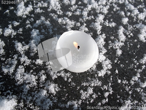 Image of white lit candle on ice