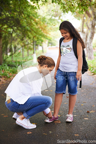 Image of Woman, teacher and tying student shoes in park for back to school, learning or education in nature. Female person teaching little girl to tie laces on asphalt path, road or outdoor street in woods