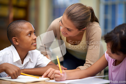 Image of Happy teacher, students and writing in classroom for education, learning or tutoring at school. Woman, mentor or educator smile for helping kids or children with books in study, library or class