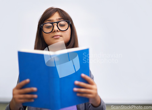 Image of Classroom, child and reading a book for knowledge, information and education by whiteboard. Girl, student and learning or studying for assessment, academy test and notebook for story and growth