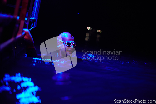 Image of authentic triathlete swimmer having a break during hard training on night neon gel light