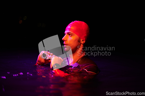 Image of Authentic triathlete swimmer having a break during hard training on night neon gel light