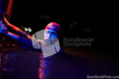 Image of authentic triathlete swimmer having a break during hard training on night neon gel light