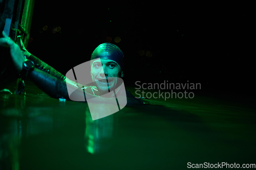 Image of authentic triathlete swimmer having a break during hard training on night neon gel light