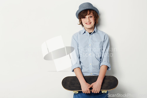 Image of Child, boy and skateboard for portrait in studio, cool clothing and confidence by white background. Happy male person, kid and hat by mockup or pride for activity, smile and trendy fashion or sport