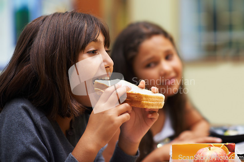 Image of Hungry girl, student and eating sandwich in classroom at school for meal, break or snack time. Young kid, person or elementary child biting bread for lunch, fiber or nutrition in class during recess