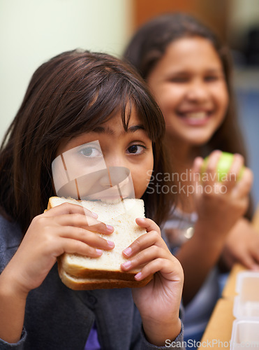 Image of Hungry girl, portrait and student eating sandwich in classroom at school for meal, break or snack time. Young kid or elementary child biting bread for lunch time, fiber or nutrition in class recess