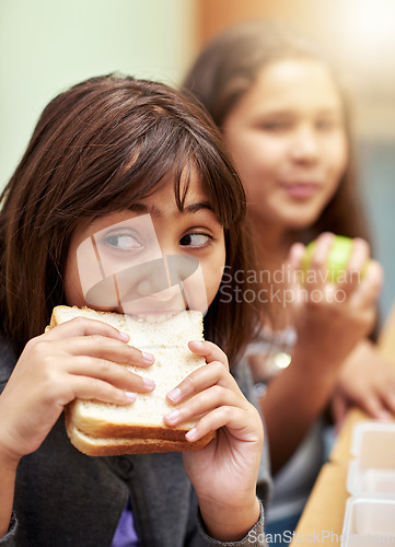 Image of Girl, face and student biting sandwich for meal, break or snack time in classroom at school. Hungry young kid or elementary child eating bread for food, fiber and nutrition in class during recess