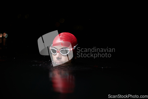 Image of A determined professional triathlete undergoes rigorous night time training in cold waters, showcasing dedication and resilience in preparation for an upcoming triathlon swim competition