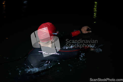 Image of A determined professional triathlete undergoes rigorous night time training in cold waters, showcasing dedication and resilience in preparation for an upcoming triathlon swim competition