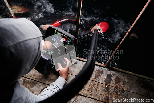 Image of Videographer taking action shot of triathlon swimming athlete at night