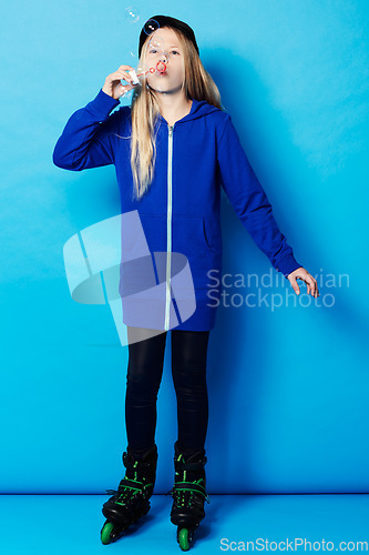 Image of Fashion, studio and child blow bubbles for fun game, activity and playing in stylish clothes isolated on blue background. Rollerblades, trendy and young kid with soap toy for leisure entertainment