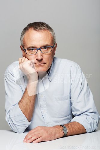 Image of Serious, portrait and senior businessman in a studio with pride for legal corporate career. Glasses, table and professional elderly male lawyer with bored face expression isolated by gray background.