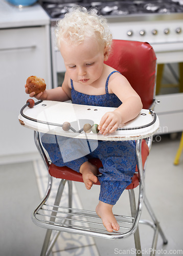 Image of Child, high chair and eating cupcake, food and breakfast sweets at home in kitchen. Young kid, hungry toddler and muffin dessert, sugar and pastry snack for cute adorable girl in house in the morning