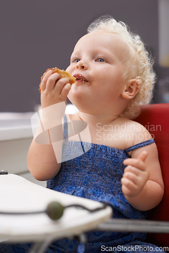 Image of Kid, high chair and eating cupcake, food and breakfast sweets at home in kitchen. Young child, hungry toddler and muffin dessert, sugar and pastry snack for cute adorable girl in house in the morning