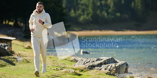 Image of Athletic man maintains his healthy lifestyle by running through the scenic mountain and lakeside environment, showcasing a commitment to fitness and well-being