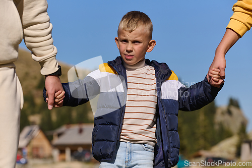 Image of A close-up shot features a young boy walking hand in hand with his parents , as they joyfully explore the wonders of nature together, creating lasting memories of familial love and outdoor adventure