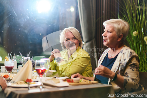 Image of Elderly friends share a delightful dinner, filled with laughter, joy, and the warmth of enduring friendship, epitomizing the timeless pleasure of companionship in a contemporary setting