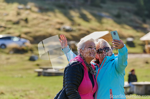Image of An elderly pair of women captures a timeless moment on their smartphones, blending technology with the serene beauty that surrounds them