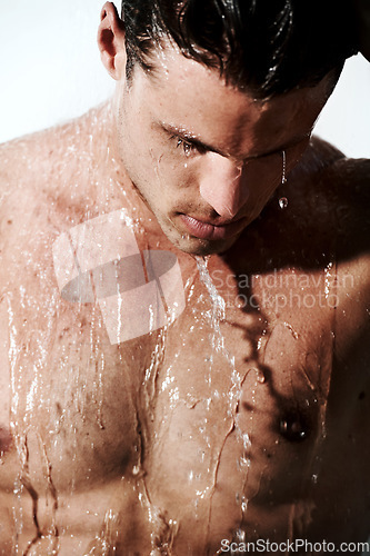 Image of Serious, man in shower to relax and washing body for hygiene, morning wellness and skin routine. Grooming, skincare and face of male model with muscle cleaning in water, self care and calm bathroom.