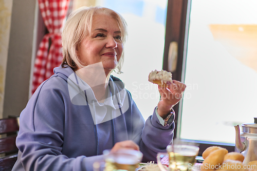 Image of Elderly woman finds pure joy in the early morning as she savors a wholesome breakfast on the porch of her rustic cottage, embracing the serenity of nature that surrounds her