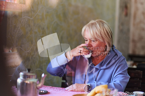 Image of Elderly woman savors the serenity of the morning as she enjoys a cup of coffee on the porch of her rustic cottage, finding solace in the simplicity of nature and contemplative moments