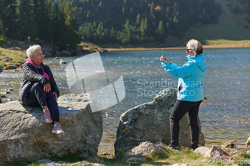 Image of An elderly pair of women captures a timeless moment on their smartphones, blending technology with the serene beauty that surrounds them