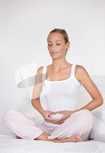 Image of Calm woman, relax and spiritual wellness on bed for health, chakra or morning wakeup at home. Young female person holding stomach or tummy in zen, meditation or awareness sitting in bedroom at house