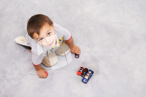 Image of Car, toys and portrait of kid playing for learning, development and fun at modern home. Cute, top view and sweet young boy child enjoying game with vehicles on floor for childhood hobby at house.