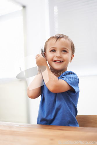 Image of Toddler, boy and phonecall in house, happiness and communication with technology. Table, cheerful and conversation for learning, cellphone and excited for child development, mobile and digital