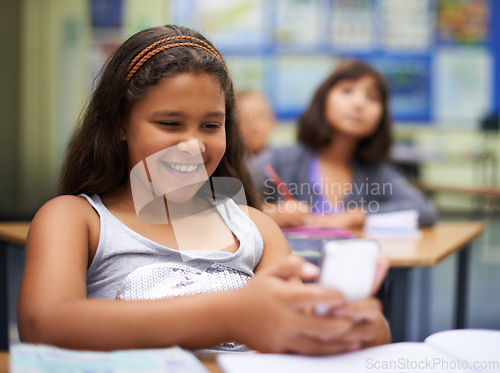 Image of School, students or girl with a phone for texting, gossip or message notification in classroom. News, sharing or happy child with a funny meme on mobile app or social media for online distraction