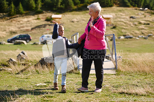 Image of Elderly grandmother and her grandchild share a leisurely stroll through nature, enveloped in the beauty of their surroundings, fostering a bond that transcends generations