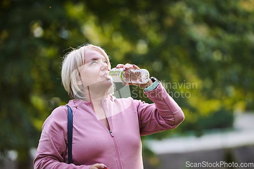 Image of An elderly woman drinks water after a hard workout in nature