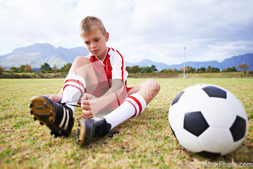 Image of Boy, soccer player and ball with shoe laces, field and ready for game, shoes and child. Outdoor, playful and sport for childhood, person and athlete for match, alone and outside on football pitch