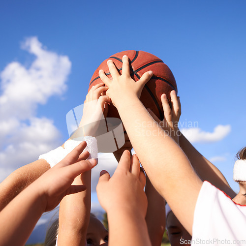 Image of People, hands and basketball in team sports for motivation, unity or community with blue sky background. Closeup group of players holding ball up in air for friendly match or outdoor game in nature