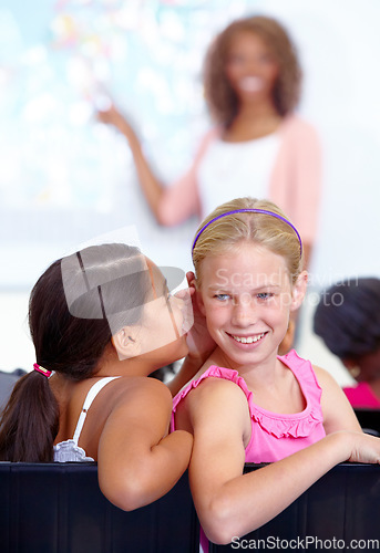 Image of Little girls, whisper and classroom in ear for secret, gossip or communication in lesson at school. Children, students or friends listening to rumor, information or class together with teacher