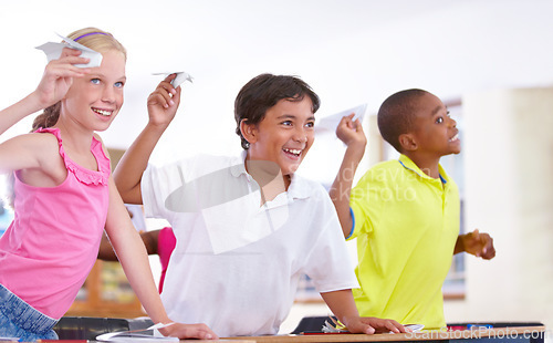 Image of Happy kids, students and paper plane in classroom on break at desk for fun games to throw or relax. Diversity, distraction or children playing with smile, origami jet or airplane in school together