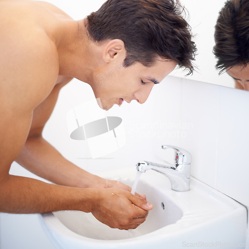 Image of Man, washing face and water for hygiene in mirror, clean and cosmetics or skincare. Male person, bathroom and wellness in morning routine, reflection and grooming or self care and basin at home