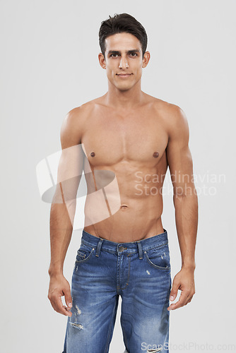 Image of Man, portrait and bodybuilder in studio for fashion, pride and confident in jeans for style. Male person, shirtless and fitness or muscle progress, face and body care or wellness by gray background