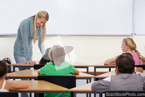 Image of Teacher, children and classroom for education, learning and writing or language development with support at desk. Happy woman with kids for teaching, helping with knowledge and questions at school
