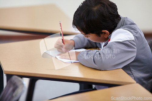 Image of Boy, school and writing in classroom with notebook, studying lesson and learning knowledge at desk. Child, student and kid drawing on paper for academic development, educational test and assessment