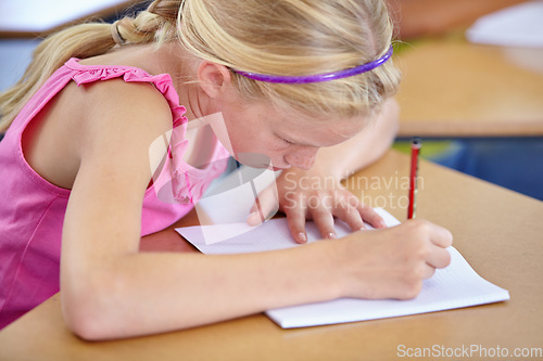 Image of Girl, school and writing in classroom with notebook, studying lesson and learning assessment at desk. Child, student and kid drawing on paper for academic development, educational test and knowledge